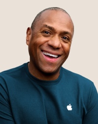 Retrato de una persona del equipo de Apple Retail sonriendo con cabello corto, gris oscuro.