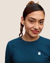Retrato de una persona del equipo de Apple Retail sonriendo con cabello largo oscuro con rayitos rosas.