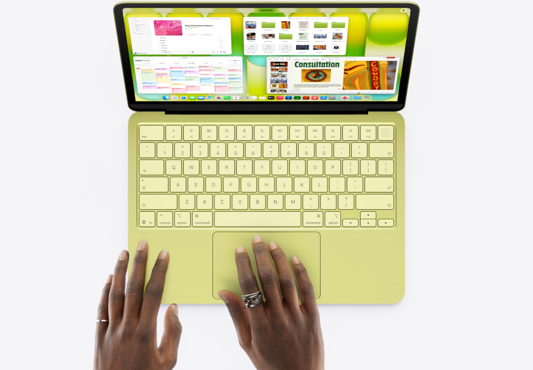 Tsitruse toonis MacBook Neo, inimese käsi puuteplaadil, avatud on mitu akent, sealhulgas rakendused Music, Calendar ja Microsoft PowerPoint