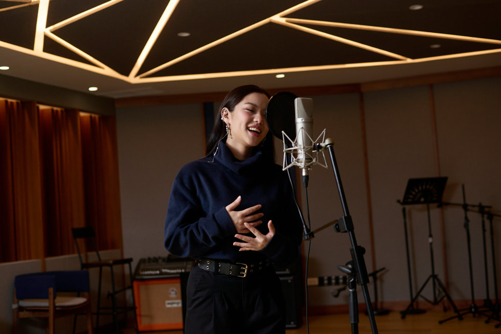 MONICA sings into a microphone in a music studio.