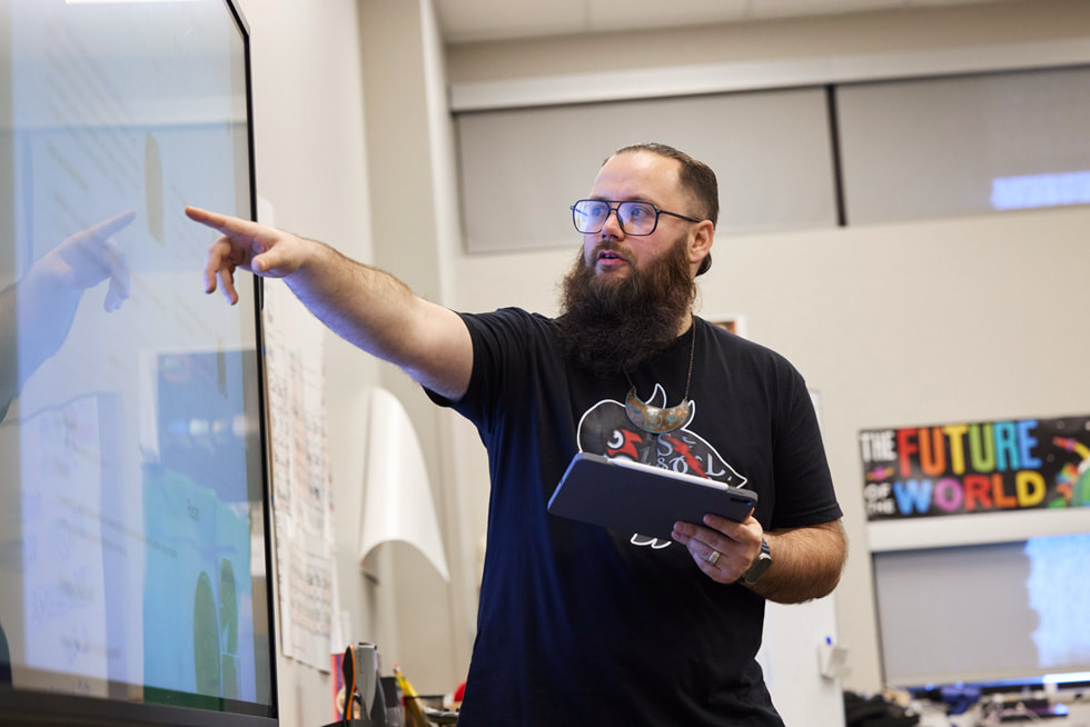Imagen de Tyler Teague sosteniendo un iPad y señalando una pantalla en un aula.