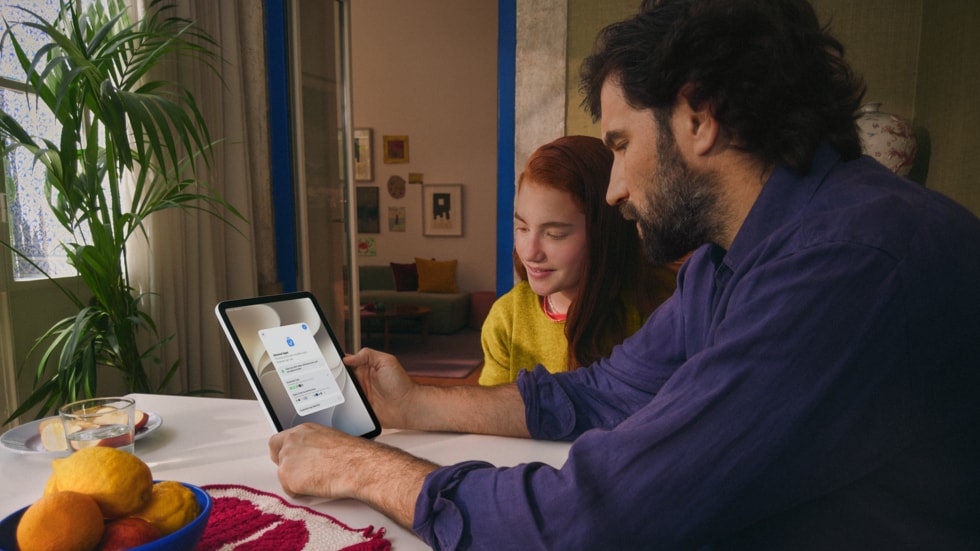Een volwassene en een kind die samen aan een houten tafel zitten en een iPad gebruiken.