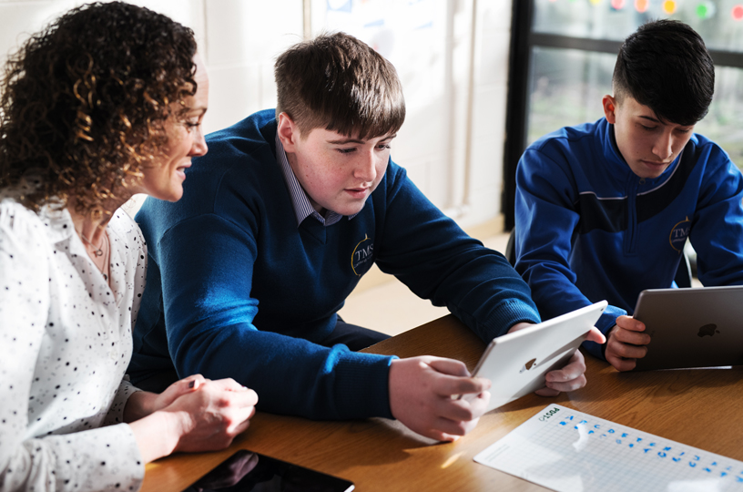 A teacher assists students using iPad to solve a cipher code.