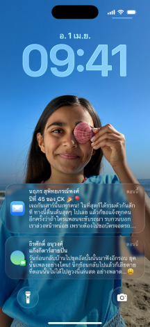 iPhone ทั้งหมด 5 รุ่นวางเรียงในลักษณะซ้อนกันเล็กน้อย ด้านซ้ายสุดแสดงการสนทนาพร้อมพื้นหลังในแอปข้อความ ถัดมาทางขวาแสดงหน้าจอโฮมพร้อมไอคอนแอปสีสันสดใส รุ่นตรงกลางแสดงหน้าจอล็อคพร้อมภาพถ่ายและตัวเลขเวลาแบบ Liquid Glass พร้อมการแจ้งเตือน 2 รายการด้านล่างของหน้าจอ ถัดไปทางขวาแสดงไอคอนแอปแบบใสในสไตล์ Liquid Glass และด้านขวาสุดแสดงเครื่องเล่นเพลงในสไตล์ Liquid Glass เช่นกัน