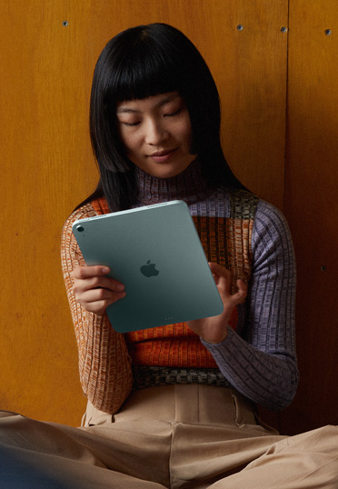 一位女學生靠牆坐在地上，手裡拿著一部 iPad
