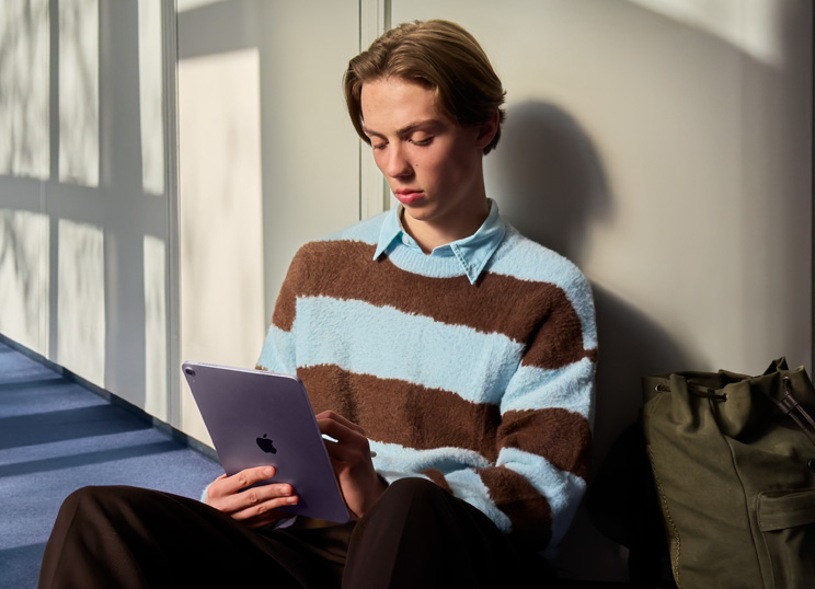 Une personne assise par terre dans une pièce lumineuse, utilisant un iPad et un Apple Pencil.