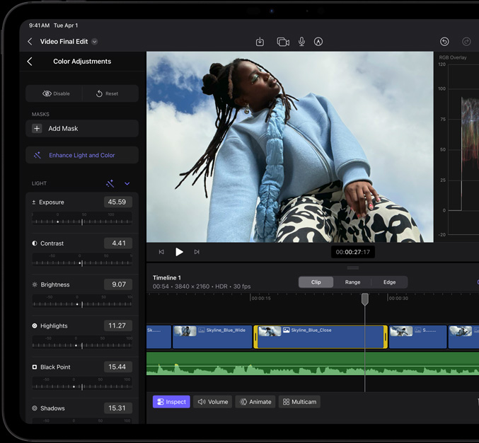 Vooraanzicht van iPad Pro, zwarte rand rond display, op het display is een app voor videobewerking te zien met een foto van een model in een blauwe jas en een zwart-witte broek, links is het paneel voor kleurcorrectie geopend met verschillende video-effecten en schuifregelaars, onderaan de tijdlijn met meerdere videofragmenten en audiosporen