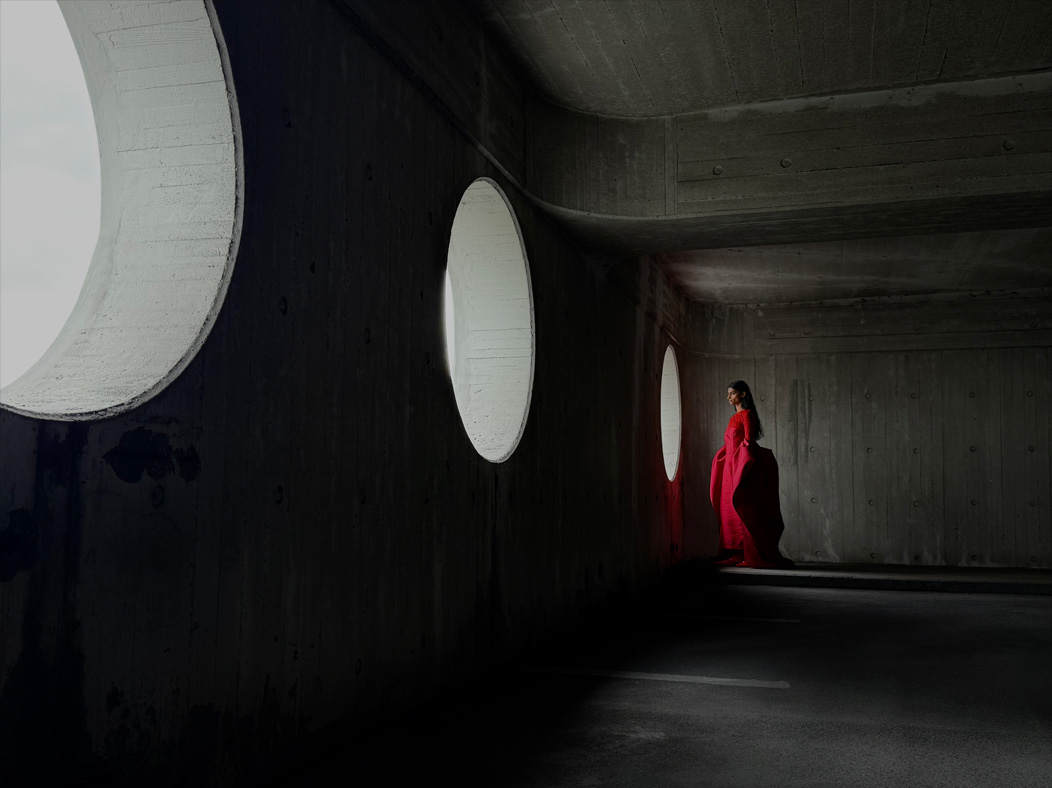 Una mujer con vestido largo rojo está siendo fotografiada de pie en una sala vacía. La distancia focal de la imagen avanza en la app Fotos para demostrar las capacidades del sistema de cámaras Pro, se muestra una distancia focal de 35 mm