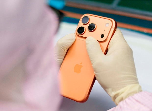Une personne en combinaison de travail intégrale inspecte un iPhone à un poste de travail